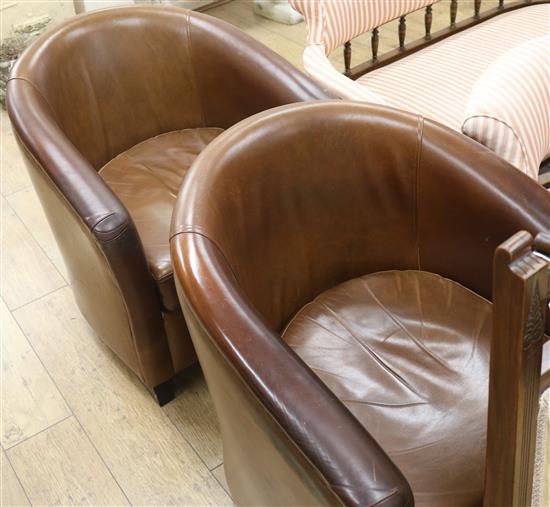 A pair of tub chairs covered in brown hide